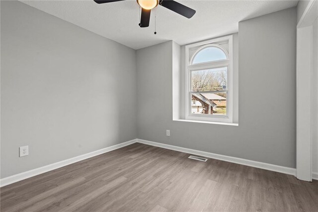unfurnished room featuring ceiling fan, visible vents, baseboards, and wood finished floors