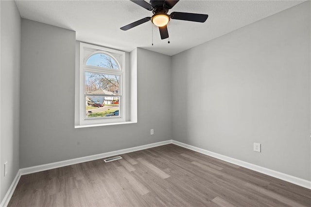 empty room with visible vents, a ceiling fan, a textured ceiling, wood finished floors, and baseboards