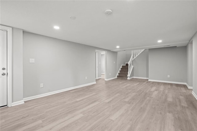 finished below grade area featuring stairs, baseboards, and light wood-type flooring