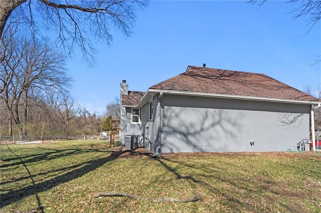 view of side of home with central air condition unit, a lawn, roof with shingles, and a chimney