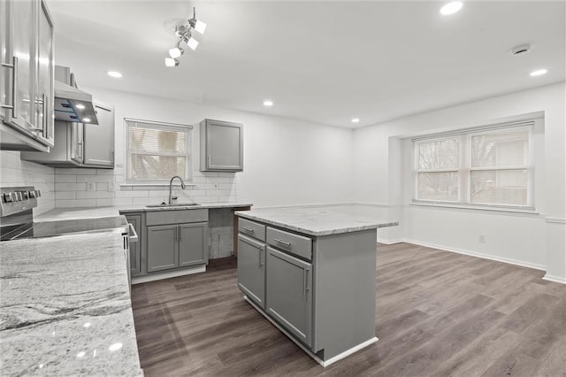 kitchen with gray cabinetry, sink, light stone countertops, and a center island