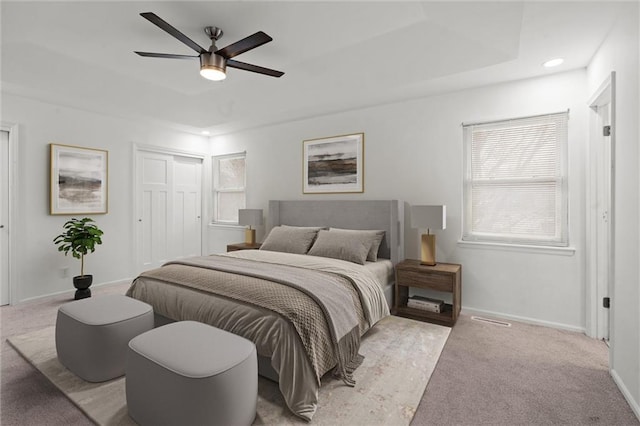 carpeted bedroom with a tray ceiling, a closet, and ceiling fan