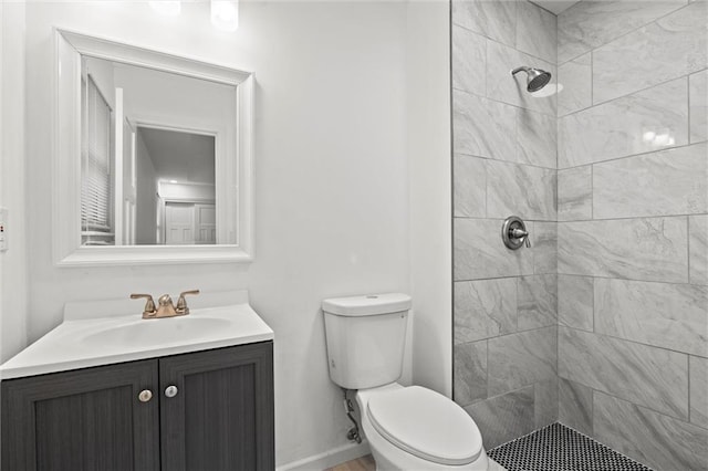 bathroom featuring baseboards, a tile shower, vanity, and toilet