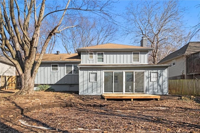 back of house with board and batten siding, a chimney, and fence