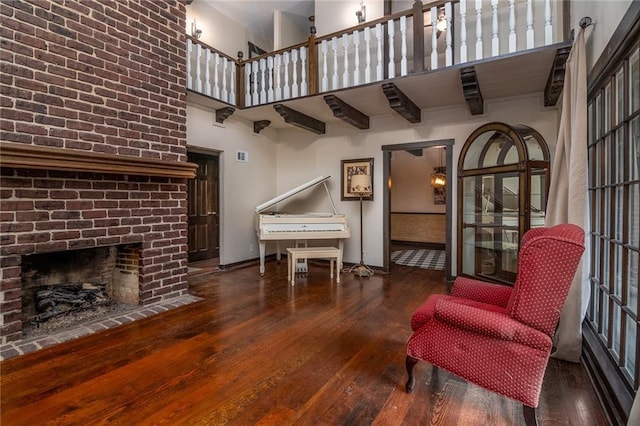 sitting room featuring a brick fireplace, dark wood-type flooring, and a towering ceiling