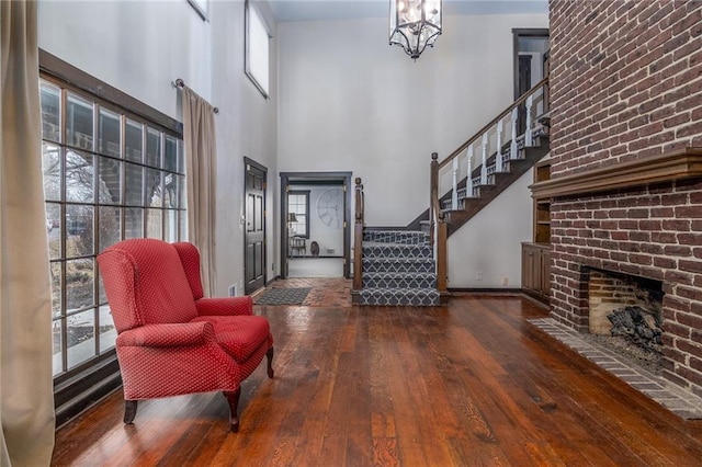 foyer featuring a brick fireplace, a towering ceiling, a notable chandelier, and dark hardwood / wood-style floors