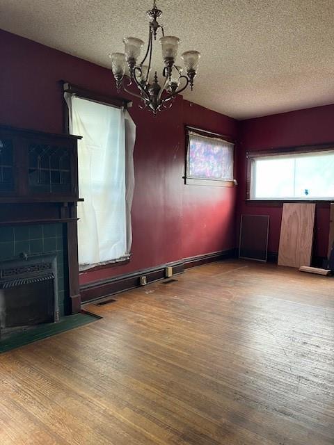 unfurnished dining area featuring a tile fireplace, hardwood / wood-style floors, a notable chandelier, and a textured ceiling