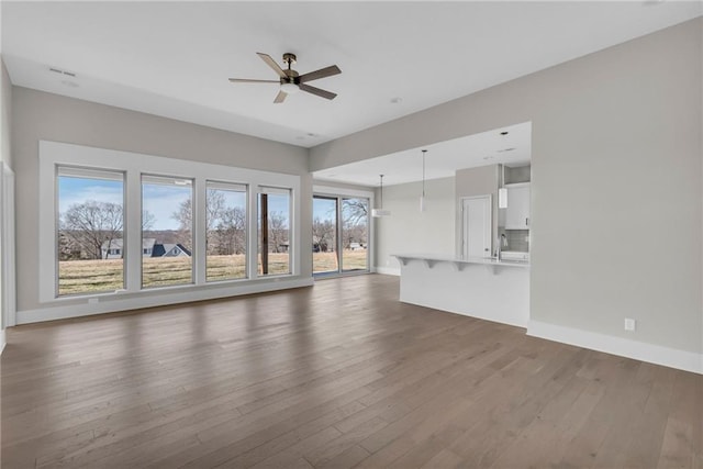 unfurnished living room featuring a ceiling fan, a sink, baseboards, and wood finished floors