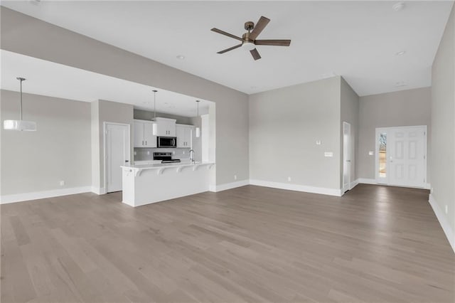 unfurnished living room with ceiling fan, baseboards, and wood finished floors