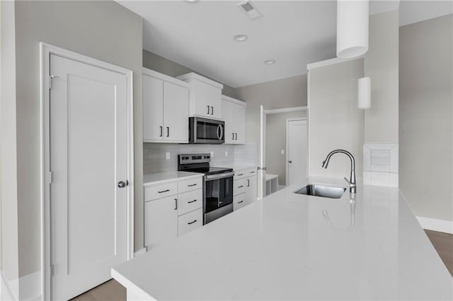 kitchen featuring white cabinets, decorative backsplash, appliances with stainless steel finishes, light countertops, and a sink