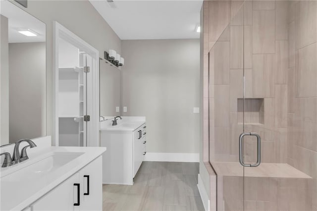 bathroom featuring a shower stall, baseboards, two vanities, and a sink