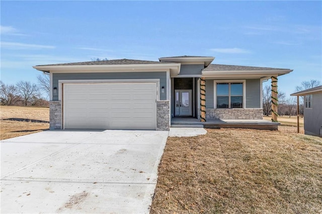 prairie-style home with a garage, stone siding, driveway, and a front lawn