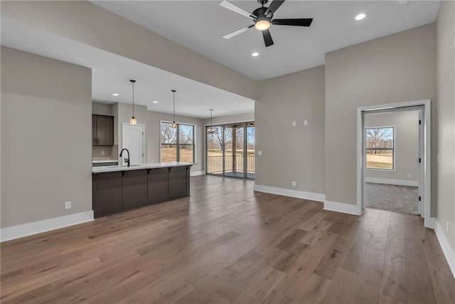 unfurnished living room featuring baseboards, recessed lighting, a sink, and light wood-style floors