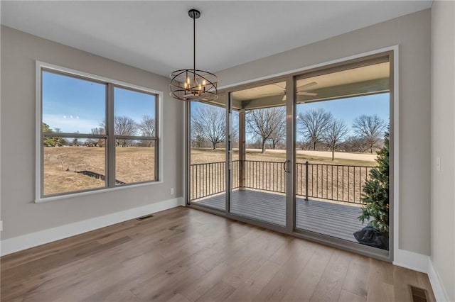 unfurnished dining area with visible vents, a notable chandelier, baseboards, and wood finished floors