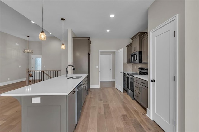 kitchen featuring light wood-style flooring, a sink, light countertops, appliances with stainless steel finishes, and decorative backsplash