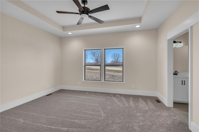 carpeted empty room with visible vents, baseboards, a raised ceiling, a sink, and recessed lighting