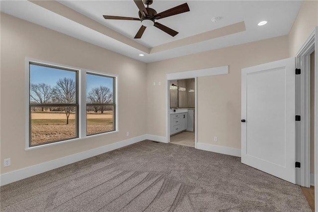 unfurnished bedroom with carpet floors, a tray ceiling, recessed lighting, ensuite bathroom, and baseboards