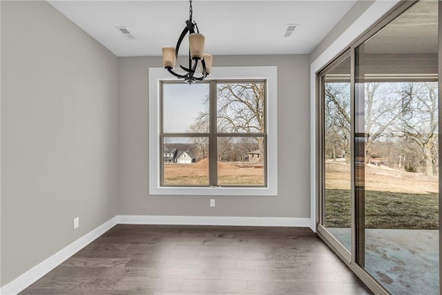 unfurnished dining area featuring an inviting chandelier, dark wood finished floors, visible vents, and baseboards