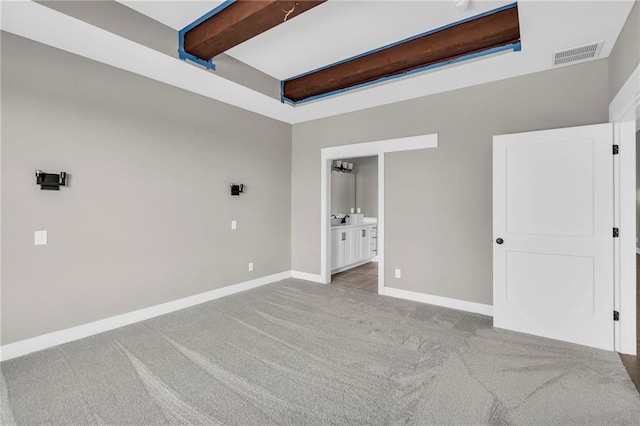 unfurnished bedroom featuring baseboards, visible vents, beamed ceiling, ensuite bathroom, and carpet floors