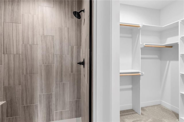 full bathroom featuring a walk in closet, a tile shower, and baseboards