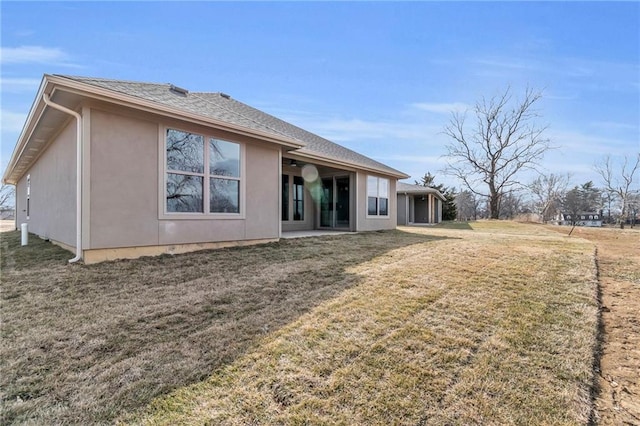 back of house featuring ceiling fan, roof with shingles, a yard, and stucco siding