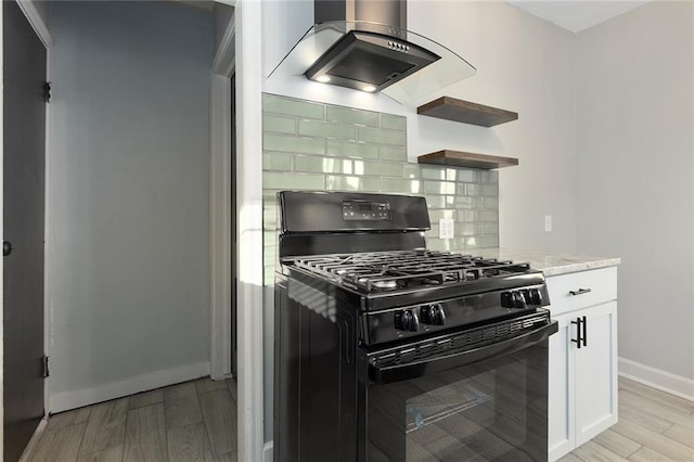 kitchen featuring black gas stove, light stone counters, island range hood, white cabinets, and decorative backsplash