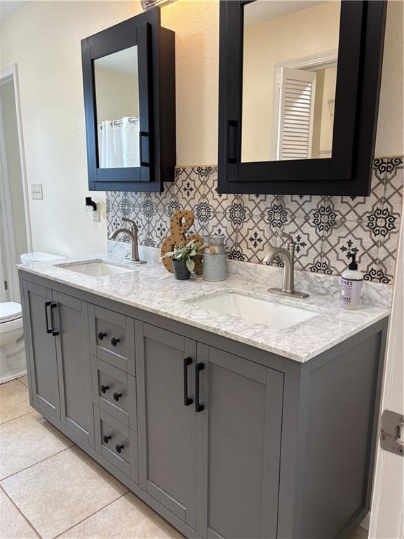 1202 NW County Road 6001, Butler, MO 64730 - full bath featuring toilet, double vanity, tasteful backsplash, and tile patterned flooring