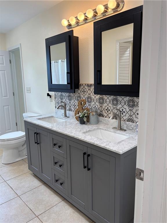 1202 NW County Road 6001, Butler, MO 64730 - bathroom featuring double vanity, tasteful backsplash, tile patterned flooring, and toilet