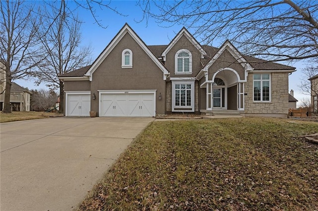 traditional home featuring stone siding, a front yard, concrete driveway, and stucco siding