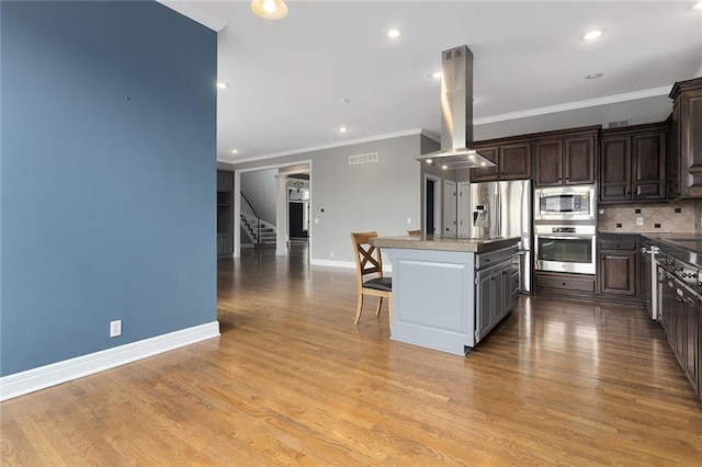 kitchen featuring dark brown cabinetry, island range hood, stainless steel appliances, visible vents, and a center island