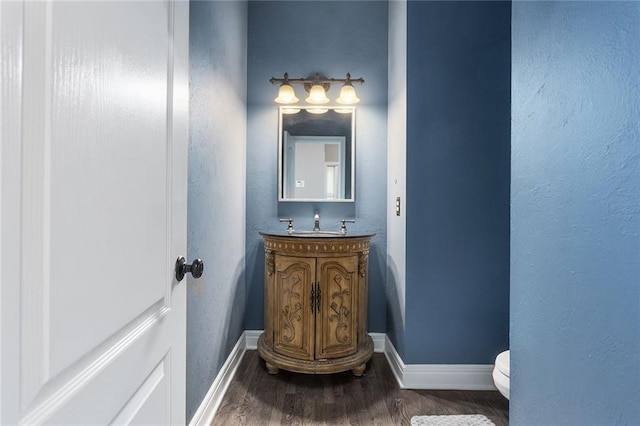 half bath with toilet, wood finished floors, vanity, and baseboards