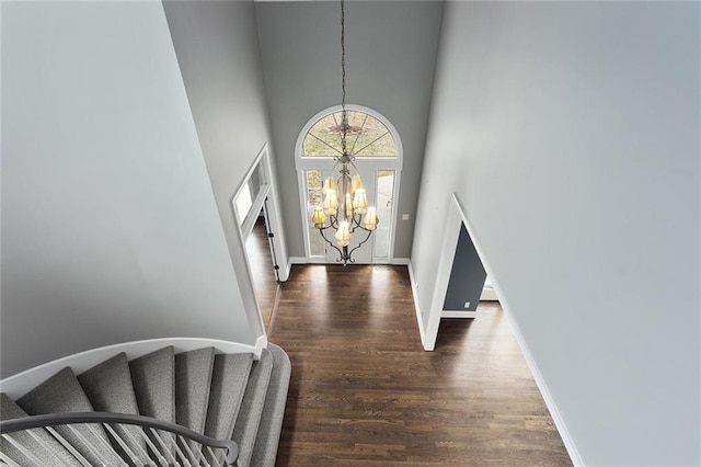 entrance foyer featuring a chandelier, wood finished floors, a towering ceiling, baseboards, and stairway