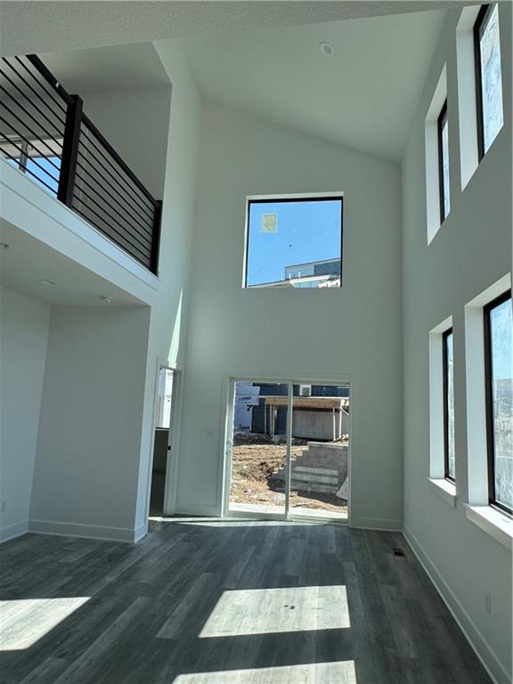 unfurnished living room featuring high vaulted ceiling, baseboards, and wood finished floors