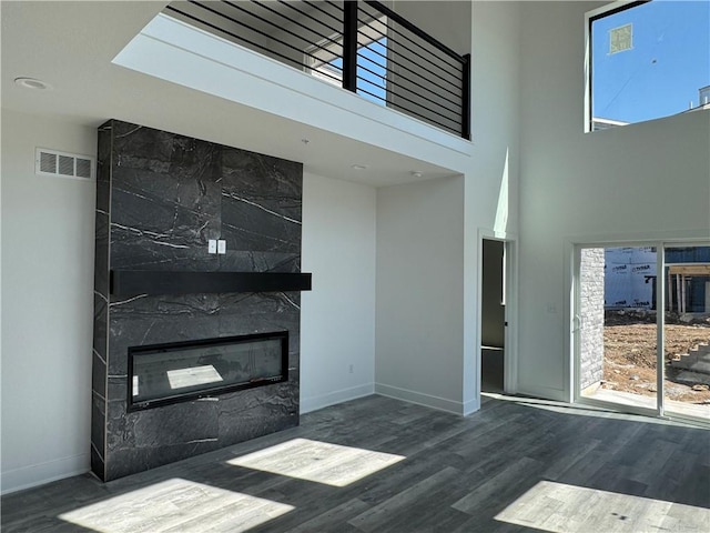 unfurnished living room featuring visible vents, wood finished floors, a fireplace, baseboards, and a towering ceiling