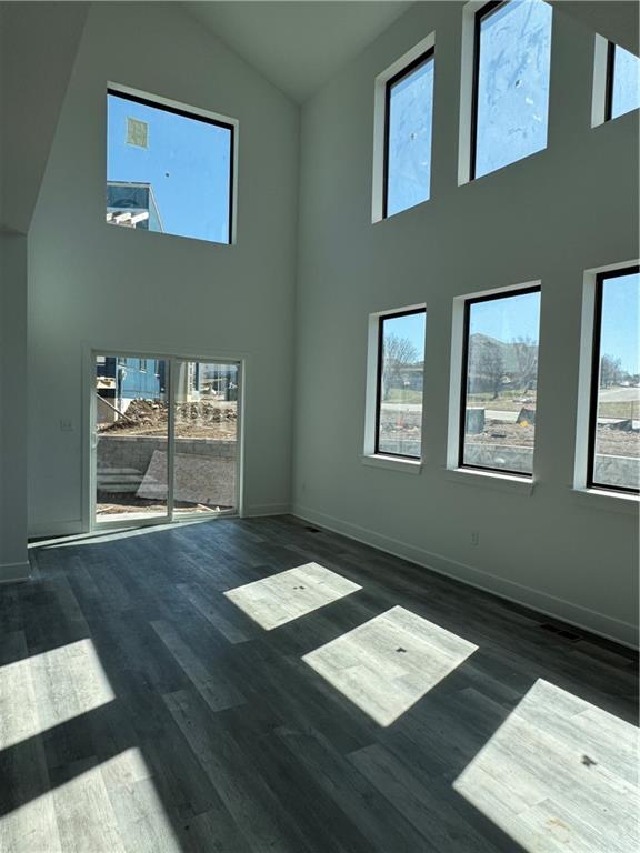 spare room featuring high vaulted ceiling, baseboards, and wood finished floors