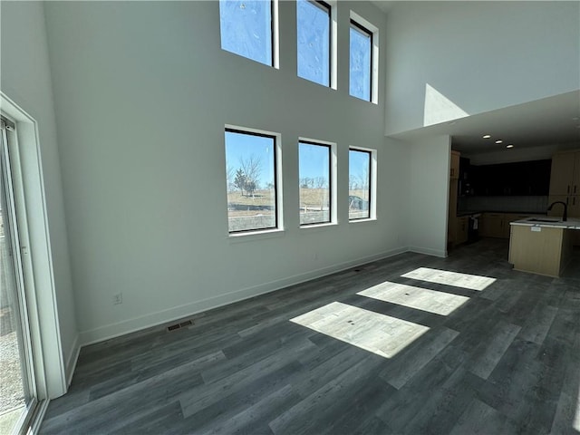 unfurnished living room with baseboards, visible vents, a high ceiling, a sink, and dark wood-type flooring