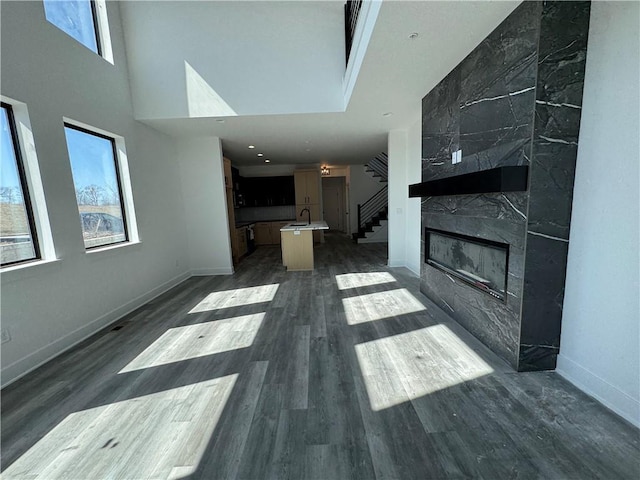 living area featuring baseboards, a high ceiling, dark wood-style flooring, a high end fireplace, and stairs