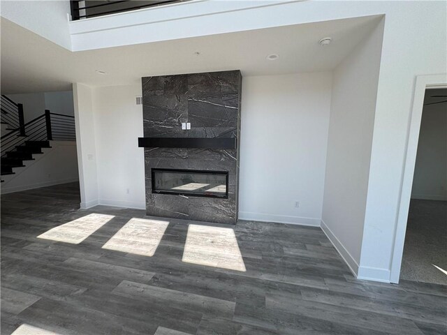 unfurnished living room with a high end fireplace, stairs, baseboards, and wood finished floors