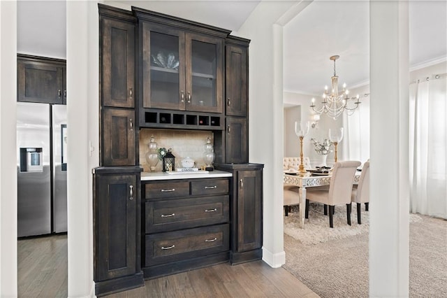 bar featuring stainless steel refrigerator with ice dispenser, tasteful backsplash, ornamental molding, and dark brown cabinets