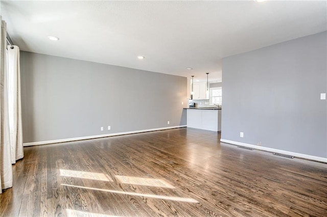 unfurnished living room featuring baseboards, dark wood-style flooring, and recessed lighting