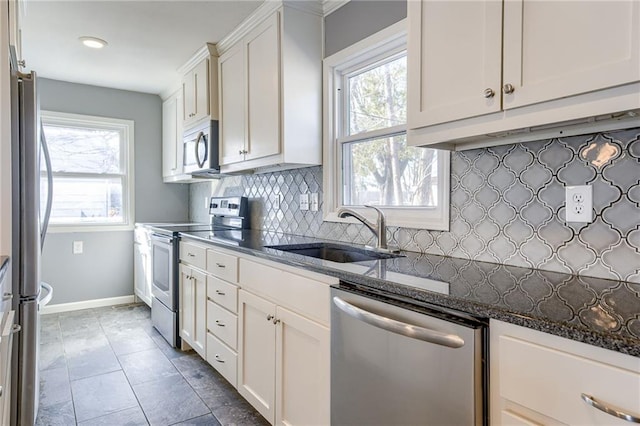 kitchen with stainless steel appliances, backsplash, white cabinetry, a sink, and dark stone counters