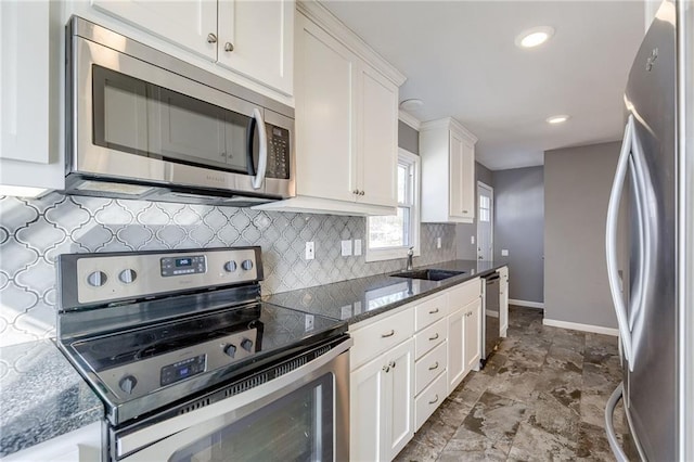 kitchen featuring baseboards, white cabinets, a sink, stainless steel appliances, and backsplash