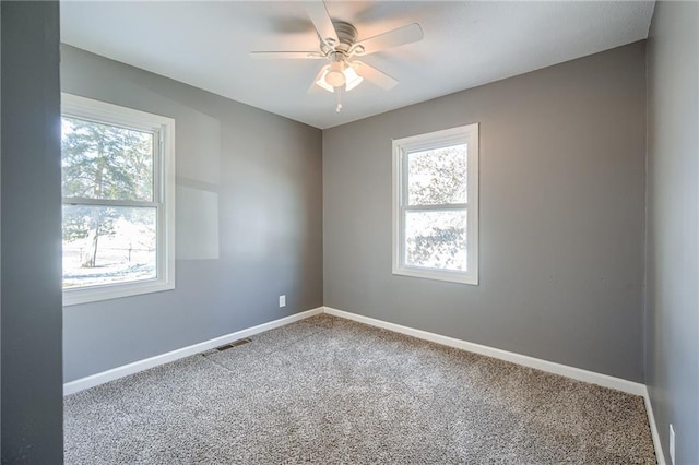 carpeted spare room featuring plenty of natural light, visible vents, and baseboards