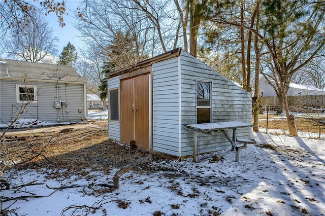 snow covered structure with a shed, an outdoor structure, and fence