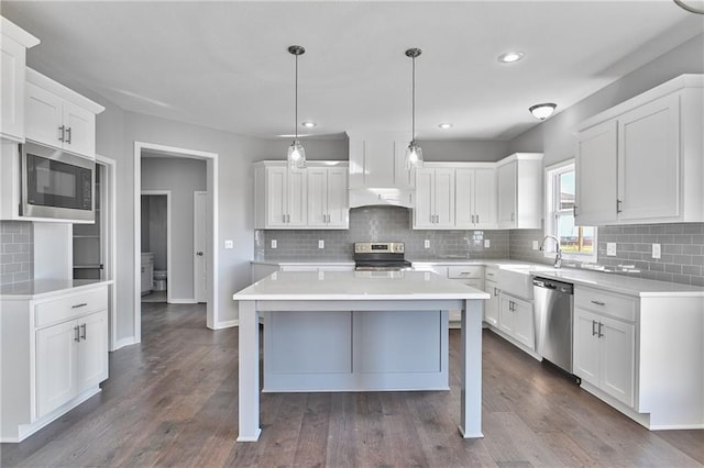 kitchen with appliances with stainless steel finishes, pendant lighting, sink, white cabinets, and a center island