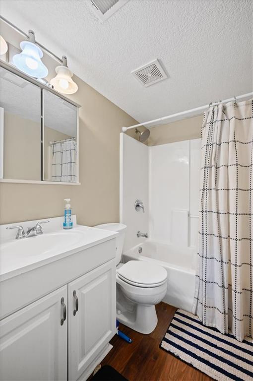 full bathroom featuring shower / bathtub combination with curtain, hardwood / wood-style flooring, a textured ceiling, and toilet