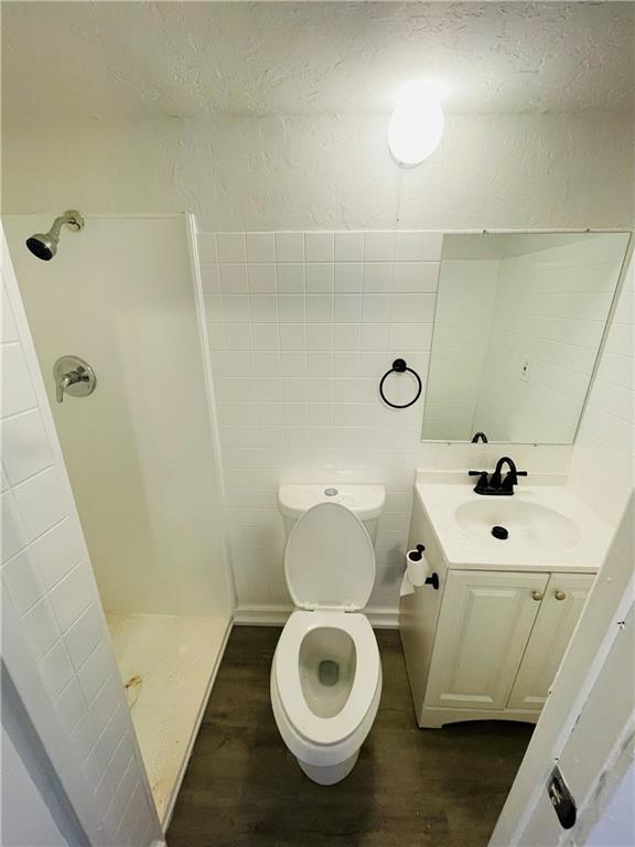 bathroom with toilet, a shower, tile walls, vanity, and hardwood / wood-style floors