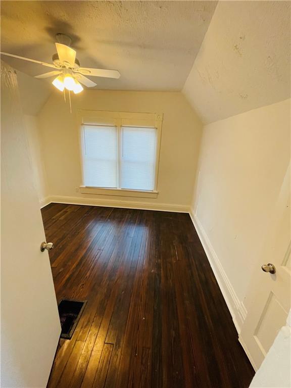 bonus room featuring lofted ceiling, ceiling fan, dark wood-type flooring, and a textured ceiling