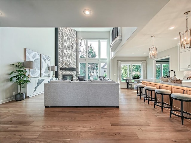 living room with a notable chandelier, a fireplace, light hardwood / wood-style floors, and a high ceiling