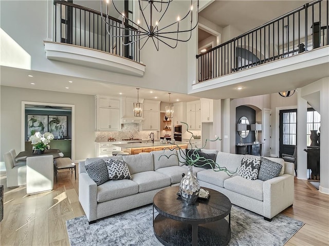 living room with an inviting chandelier, sink, light hardwood / wood-style flooring, and a high ceiling